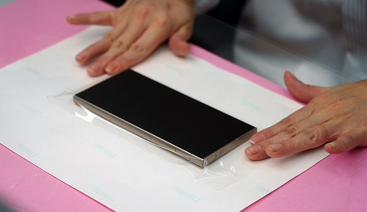 由於 HAO 5D 果凍膠玻璃保護貼需要透過果凍膠進行玻璃貼與螢幕的貼合，在施工前師傅會透過透明膠膜包覆機身正面來隔絕果凍膠與機身上的孔洞，以避免膠水溢入影響手機功能。