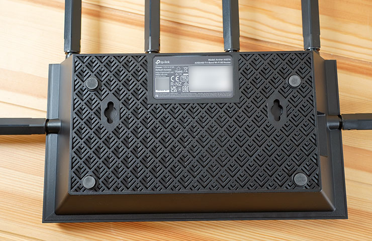 機身底部同樣有大面積的散熱孔，而且造型正頂部相同，很有一體感，同時也設計有適合置放平面的止滑墊與預留的壁掛孔，這裡的標籤同樣標示了預設連結使用的 SSID 與密碼。